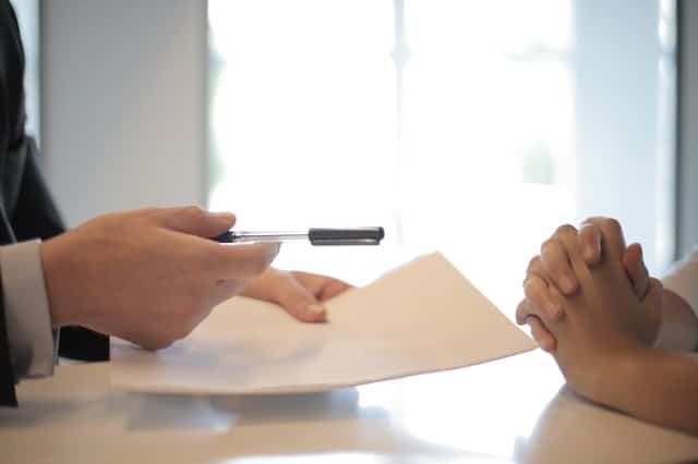 Person handing pen and paper to another person